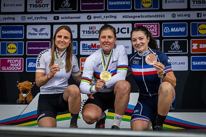 Nathalie Schneitter gewinnt E-Mountainbke Weltmeisterschaft. Drei Frau in Radsportkleidern knien für ein Foto und halten Medaillen in den Händen.