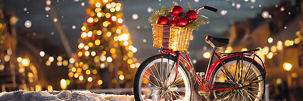 Velojournal Adventskalender Weihnachtliches Velo mit Geschenkkorb vor Christbaum und Lichtern.