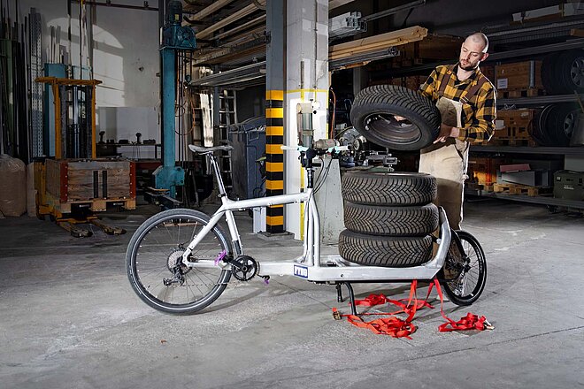 Cargobikes im professionellen Einsatz. Ein Mann lädet Autoersatzreifen auf ein Lastenrad.