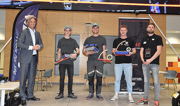 Fünf Männer stehen nebeneinander. Drei Männner haben Trophäen in der Hand.