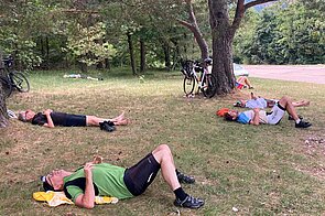 Männer in Rennradkleidung ruhen sich liegend auf einer Wiese aus