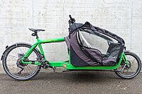 Bullitt Cargobike Test. Ein grünes Lastenrad steht vor einer Betonwand.