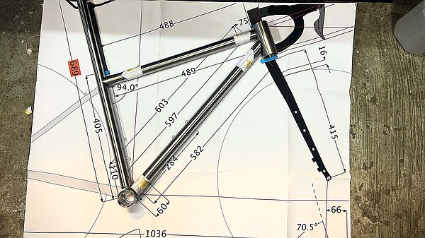 Teile eines Fahrradrahmens liegen auf einer Skizze auf einem Tisch.