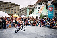 Zuschauer stehen auf einem Platz und beobachten einen Mann auf einem BMX-Rad.