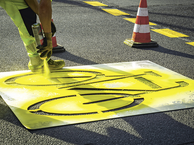Ein Arbeiter sprüht ein gelbes Velossymbol auf die Strasse