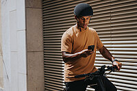 Bosch eBike Flow App Update. Ein Mann mit orangem T-Shirt sitzt auf einem E-Bike und hält ein Smartphone in der Hand.