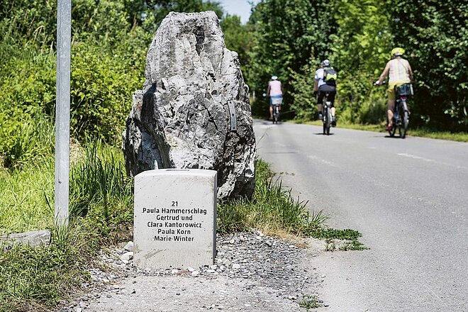 Ein Radweg bildet beim Projekt «Über die Grenze» die Erzählachse. Entlang der Vorarlberger Radroute Nr. 1 erinnern 52 Hörstationen an Fluchtgeschichten von 1938 bis 1945. Stein mit Tafel neben einem Radweg.