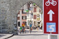 Veloverkehr Schweiz Veloland 2022. Velofahrer passieren ein Tor in einer Altstadt.