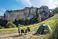 Im Mai 2021 schwingt sich  die Journalistin Susanne Brüsch  in Andalusien auf den Sattel ihres E-Bikes und «surft» auf der Öffnungswelle  nach dem Corona-Lockdown vom Atlantik bis an den Rhein. Eine Frau steht auf einer Wiese vor ihrem Zelt. 