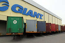 Lagerhalle mit Containern im Vordergrund. 