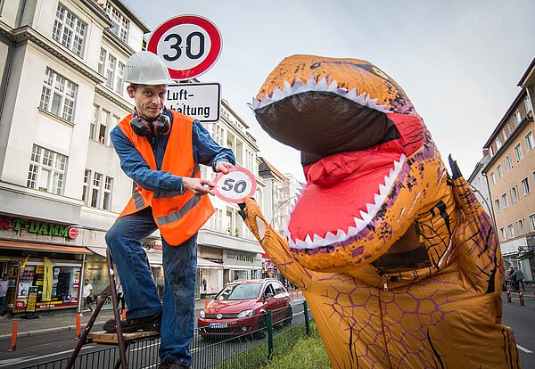 Ein Mann mit Leuchtweste und Helm hängt an Verkehrsschild auf. 