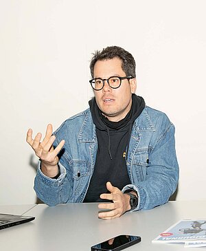 Ein Mann mit blauer Jeansjacke sitzt an einem Tisch