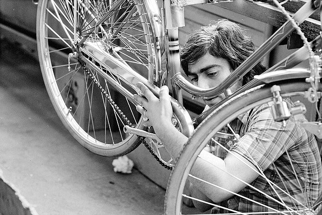 Fahrradwerkstätten im Wandel der Zeit. Schwarz Weiss Foto eines Mannes, der ein Fahrrad repariert.