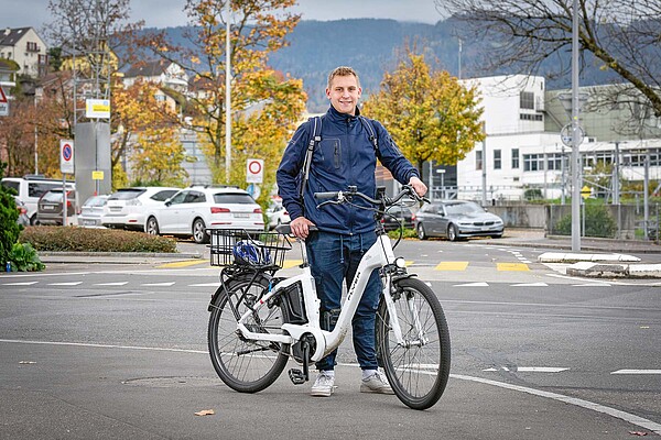 Ein Mann mit blauer Jacke steht hinter einem weissen E-Bike. 