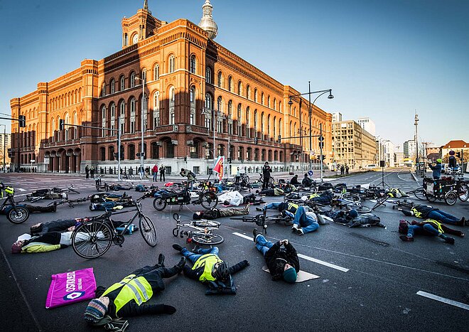 Menschen mit gelben Westen liegen auf einer Strasse am Boden. 