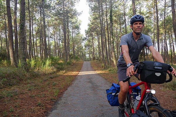 Ein Radfahrer fährt auf einem Radweg in Frankreich durch ein Waldstück..