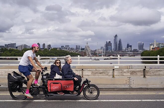 Ein Mann transportiert zwei Personen auf einem Cargobike durch London