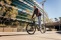 älterer Herr fährt sportlich auf einem  E-Bike entlang eines modernen Gebäudes