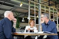 Drei Personen sitzen an einem Tisch.