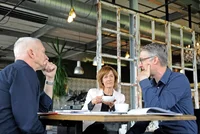 Drei Personen sitzen an einem Tisch.