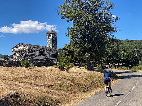 Rennradfahren in Korsika. Alte Kirche an einer Strasse.