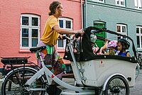 Frau mit Cargobike und Kindern vor bunter Häuserzeile