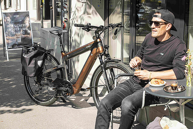 TVS Motor übernimmt M-Way. Ein Mann mit dunkler Sonnenbrille und Baseballcap sitzt in einem Café.