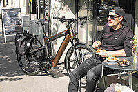 TVS Motor übernimmt M-Way. Ein Mann mit dunkler Sonnenbrille und Baseballcap sitzt in einem Café.