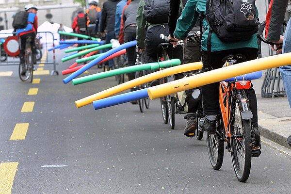 Radfahrer demonstrieren mit Badenudeln auf dem Gepäckträger für mehr Abstand beim Überholen.