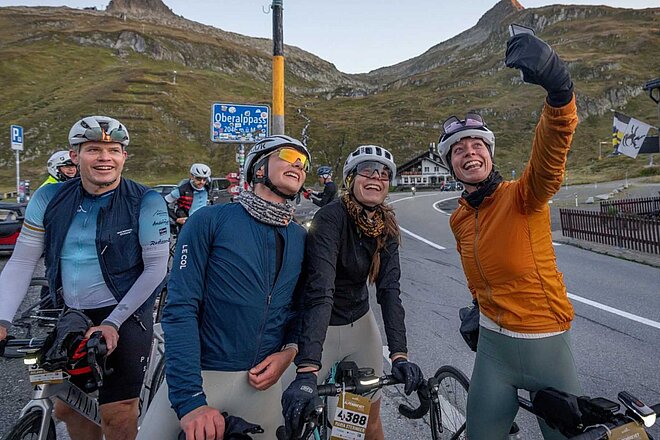 Eine Rennradfahrerin macht ein Selfie vor dem Schild eines Alpenpasses.
