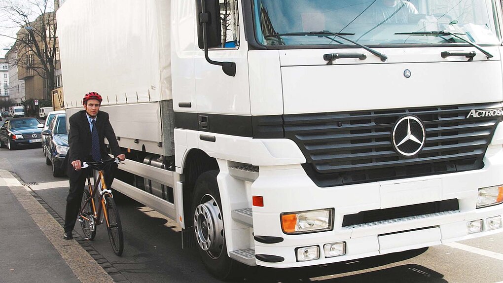 Ein Radfahrer steht am Strassenrand neben einem LKW.