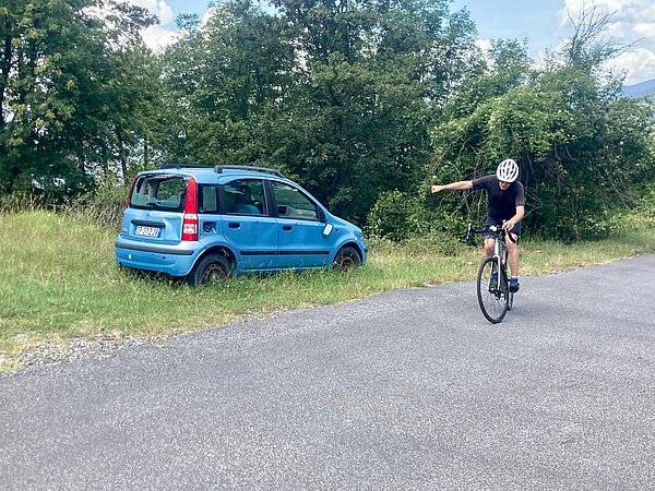 Ein kaputtes blaues Auto steht an einem Strassenrand.