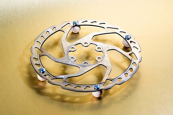 Pfannenuntersetzer aus Scheibenbremse mit Holzperlen vor goldenem Hintergund