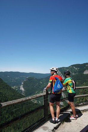 Zwei Männer in Rennvelobekleidung blicken von einem Aussichtspunkt ins Tal