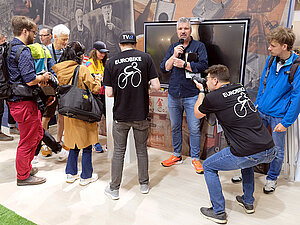 100 Jahre Abus. Journalisten mit Kameras stehen vor einem Messestand.