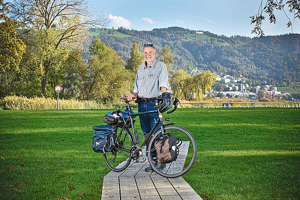 Ein Mann steht hinter seinen Fahrrad auf einer Wiese.