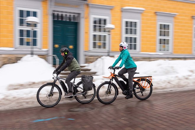 Zwei Personen fahren mit E-Bikes auf einer winterlichen Strasse