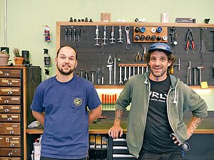 Zwei Männer stehen vor einer Werkbank in einem Fahrradgeschäft.