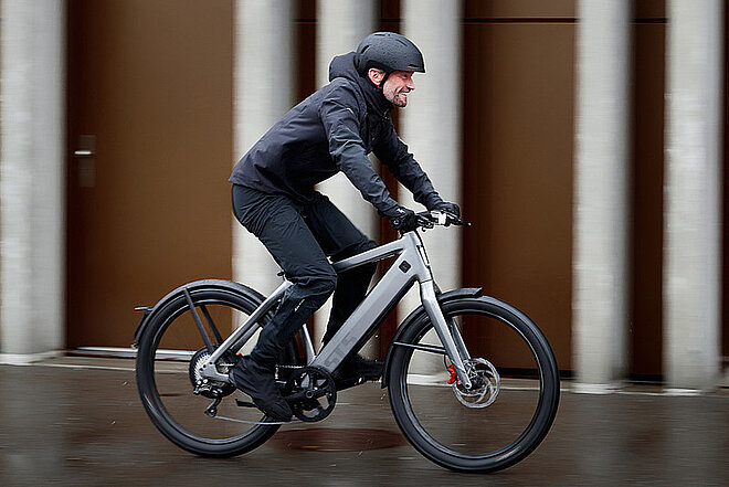 ZIV Studie Speed-Pedelecs. Ein Mann mit Regenbekleidung fährt auf einem E-Bike.