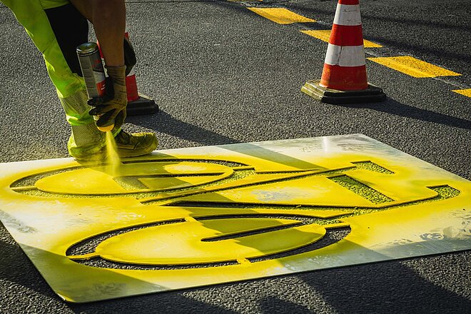 Prix Velo Infrastruktur 2024 für die Stadt Lausanne. Eine Person sprüht eine Fahrradsymbol mit gelber Farbe auf den Boden.