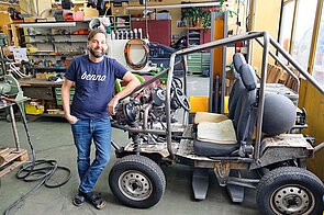 Benno Bikes Portrait. Ein Mann steht in einer Werkstatt neben einem Fahrzeug.