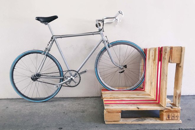 Ein Fahrrad steht in einem Veloständer aus alten Paletten.