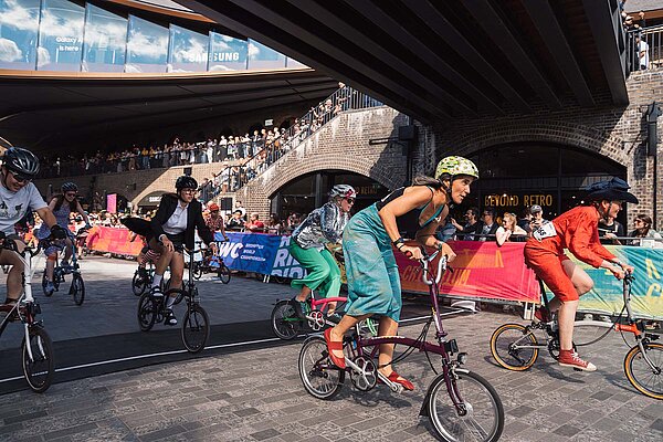 Brompton Faltvelo Rennen 2024. Eine Frau mit Kleid fährt auf einem Faltrad von Brompton.