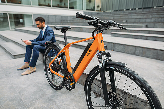 Qwic E-Bike Firmenpleite. Ein Mann im Anzug sitzt auf einer Treppe. Neben ihm steht ein E-Bike. 