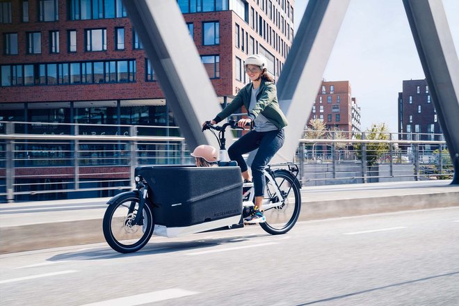 E-Bikes 2023. Die besten Modelle des Jahres. Eine Frau transportiert ein Kind auf einem Cargobike von Riese & Müller.