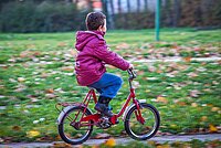 Kind mit pinker Jacke auf rotem Velo fährt einer Wiese entlang.