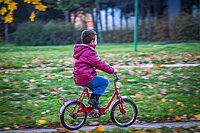 Kind mit pinker Jacke auf rotem Velo fährt einer Wiese entlang.