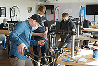 Drei Männer mit Nasenmundschutz führen Servicearbeiten an einem Fahrrad aus.