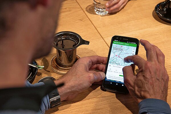 Ein Mann hält ein Smartphone in der Hand. Auf dem Bildschirm ist ein Kartenausschnitt zu sehen.