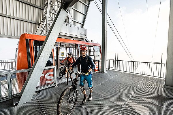 Zwei Biker steigen aus einer Gondel aus.